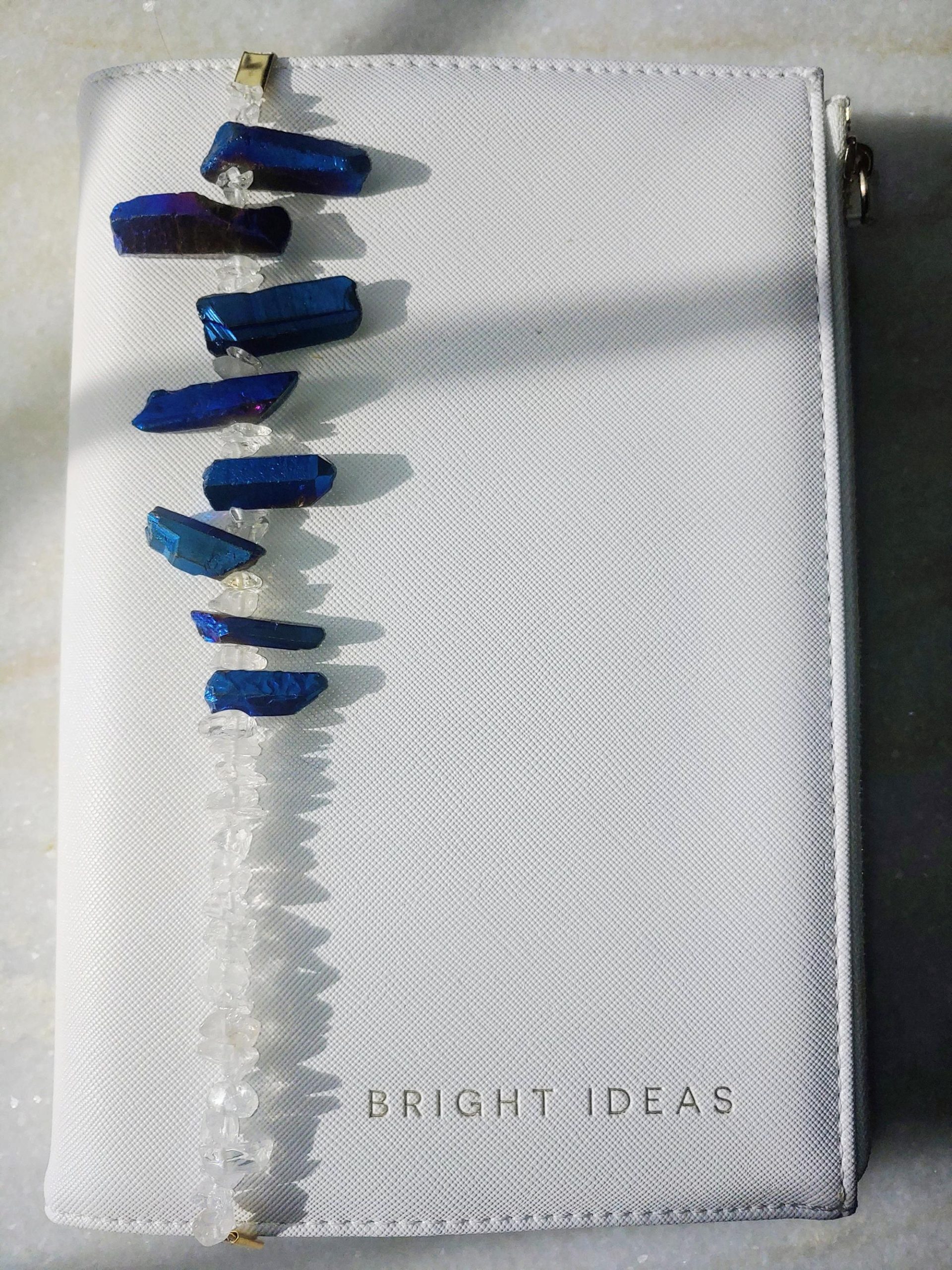 Venus bookmark from Inanna Joy Boutique, handcrafted with deep blue crystal quartz and clear gemstone chips, styled on a white "Bright Ideas" journal cover.
