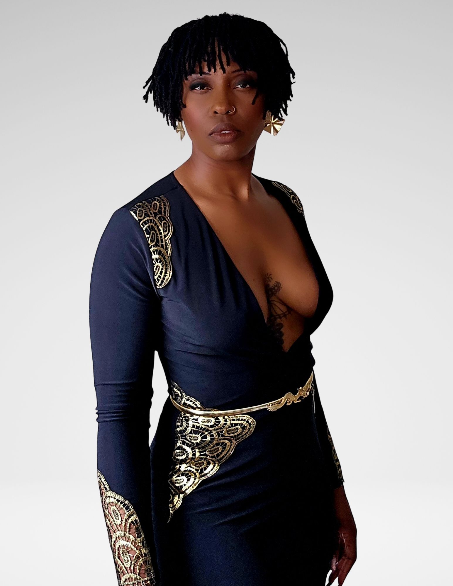 Inanna Joy wearing an elegant black and gold gown, standing confidently against a neutral background, representing strength and inspiration.